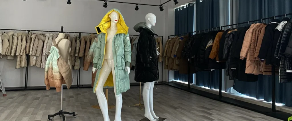 Showroom mannequins displaying a pastel mint down coat and a black quilted jacket surrounded by clothing racks