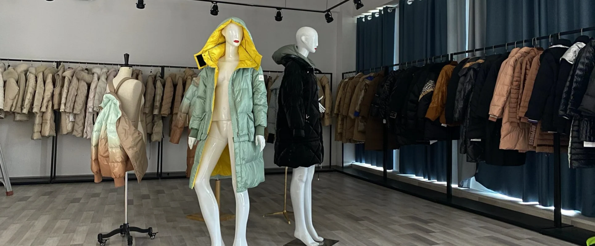 Showroom mannequins displaying a pastel mint down coat and a black quilted jacket surrounded by clothing racks
