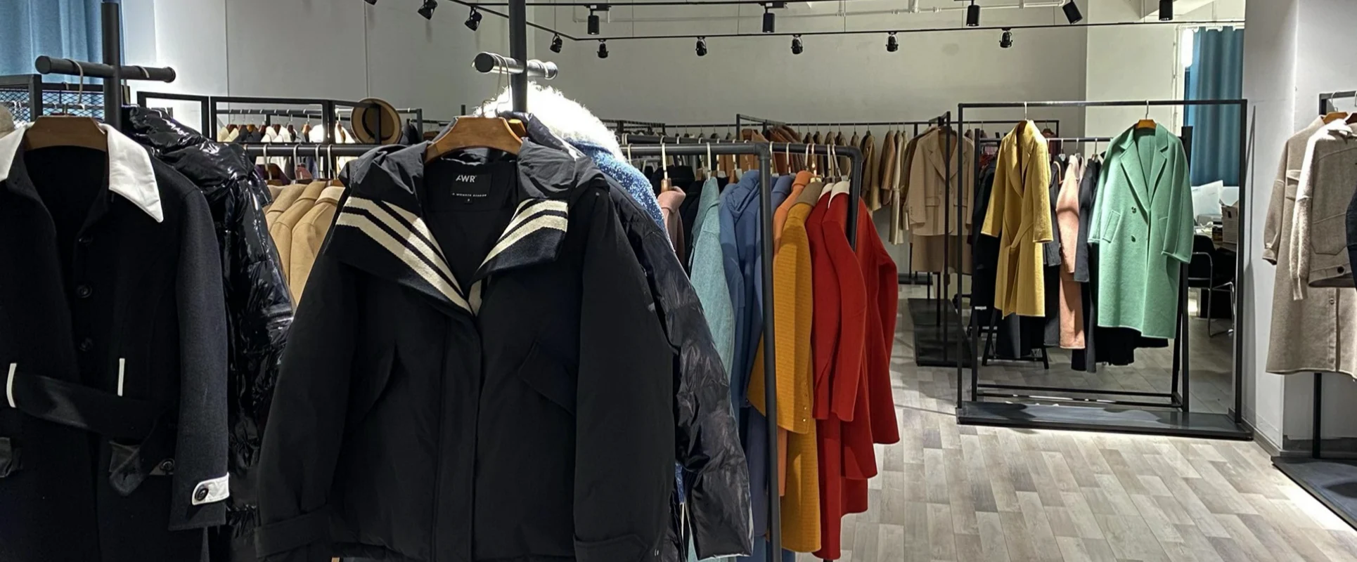 Close-up view of premium hooded winter jackets and colorful wool overcoats neatly hung on black showroom racks