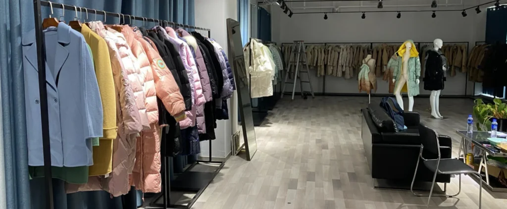 Spacious clothing showroom featuring a black leather sofa next to long rows of winter down coats and pastel trench coats