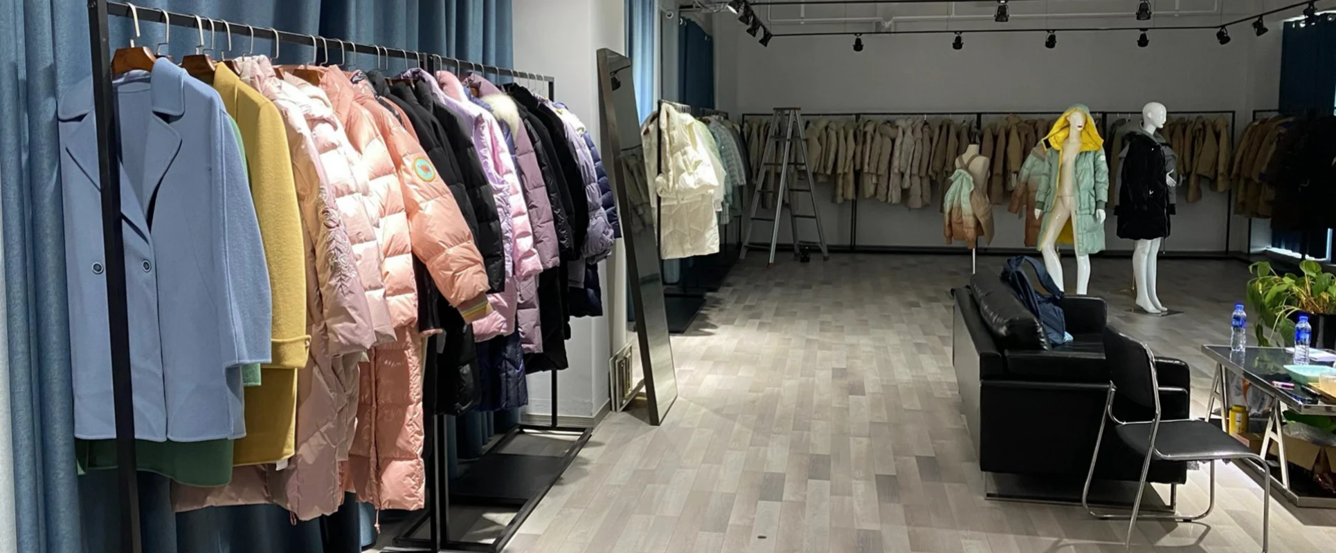 Spacious clothing showroom featuring a black leather sofa next to long rows of winter down coats and pastel trench coats