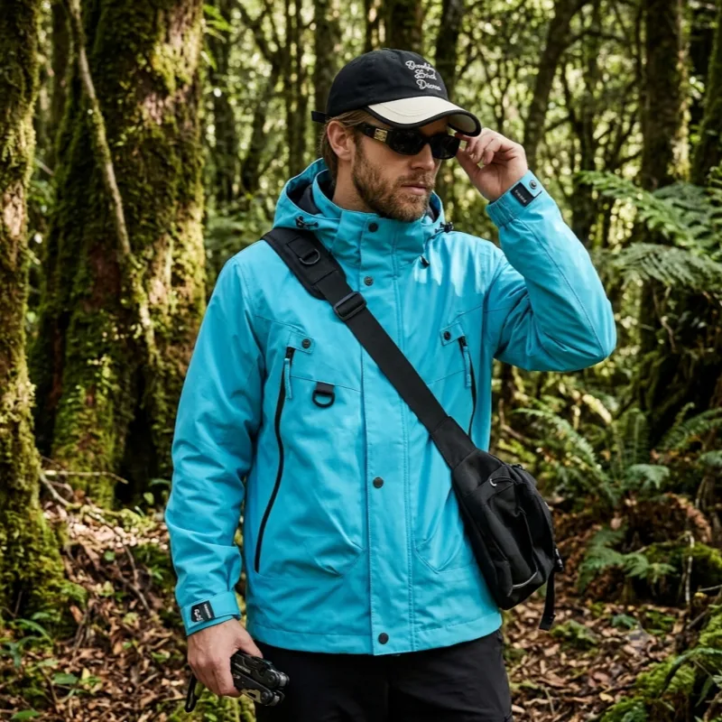 A male model wearing a technical cyan blue waterproof hardshell jacket and baseball cap hiking through a lush green forest