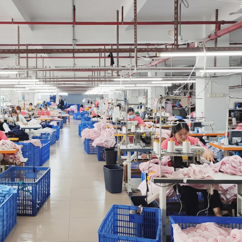 Garment factory workshop floor showing operators at sewing machine stations assembling pink clothing