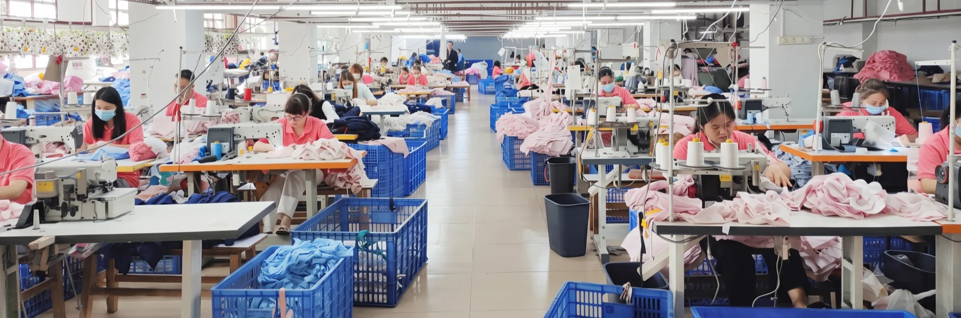 Garment manufacturing workshop with professional workers operating industrial sewing machines for bulk clothing production.
